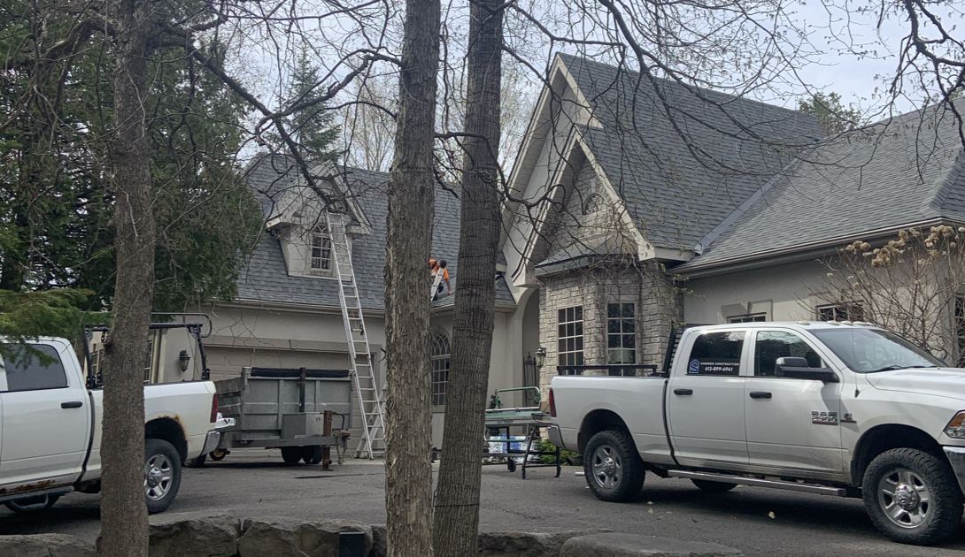 Two Sherrer Construction trucks and a ladder on the job at a stone house